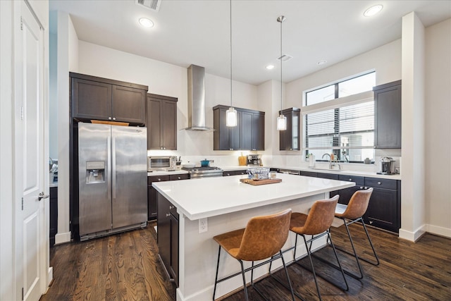 kitchen featuring stainless steel appliances, wall chimney range hood, pendant lighting, a kitchen bar, and a kitchen island