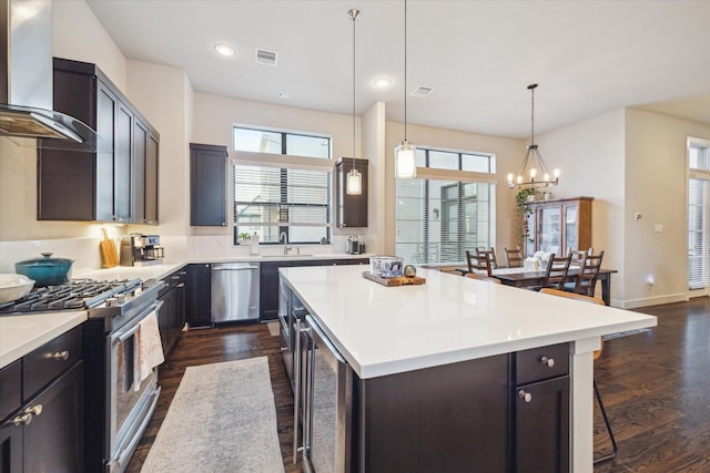 kitchen featuring a kitchen bar, stainless steel appliances, a kitchen island, and wall chimney range hood