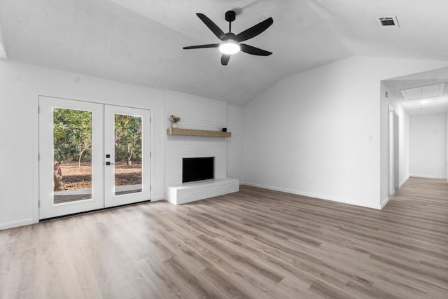 unfurnished living room featuring ceiling fan, french doors, lofted ceiling, a fireplace, and light wood-type flooring