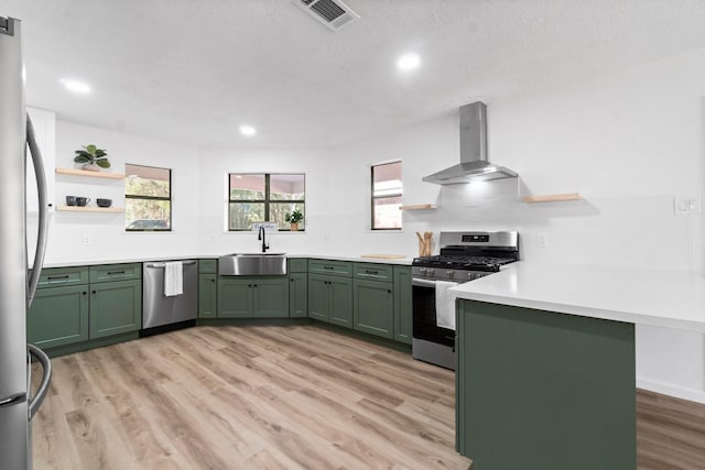 kitchen featuring kitchen peninsula, appliances with stainless steel finishes, green cabinets, and wall chimney range hood