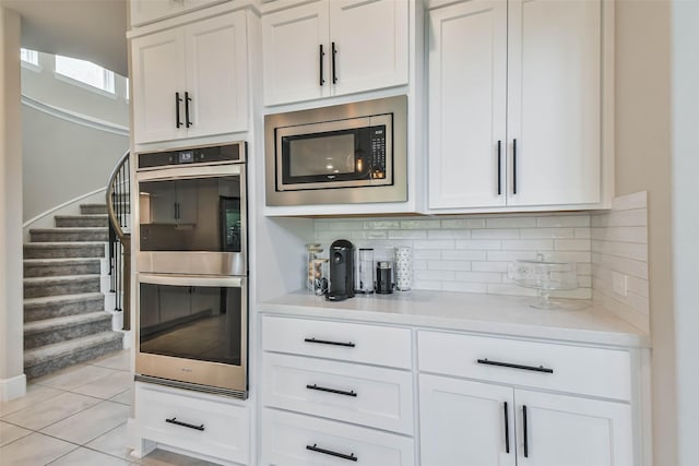 kitchen with white cabinets, light tile patterned floors, backsplash, and appliances with stainless steel finishes