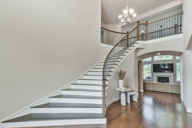 staircase featuring a towering ceiling, an inviting chandelier, and hardwood / wood-style flooring