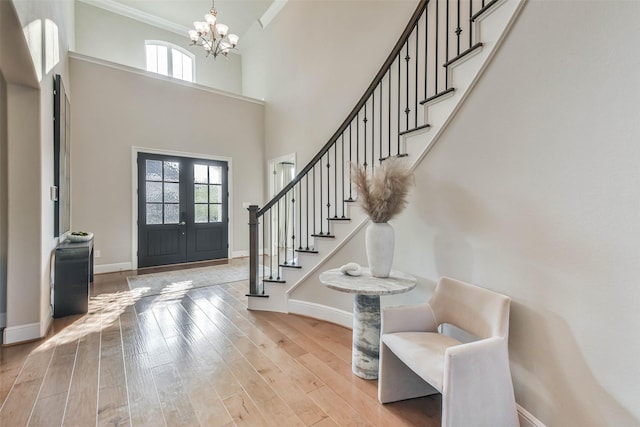 entrance foyer featuring french doors, light wood-type flooring, crown molding, an inviting chandelier, and a high ceiling