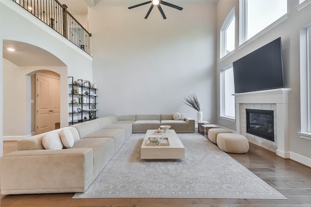 living room featuring a tiled fireplace, ceiling fan, a towering ceiling, and hardwood / wood-style flooring