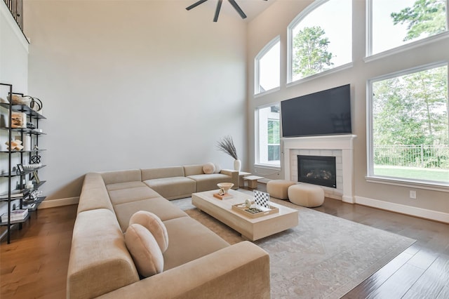 living room with a tile fireplace, a high ceiling, dark hardwood / wood-style flooring, and ceiling fan