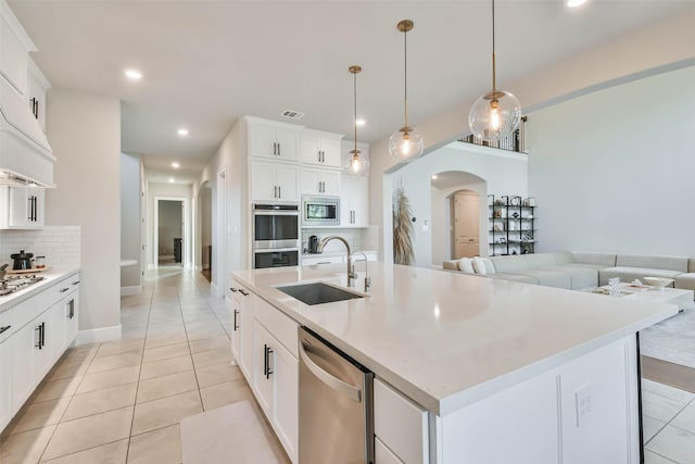 kitchen featuring stainless steel appliances, a kitchen island with sink, sink, white cabinets, and hanging light fixtures