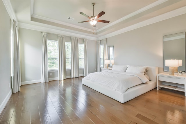 bedroom with hardwood / wood-style flooring, ceiling fan, crown molding, and a tray ceiling