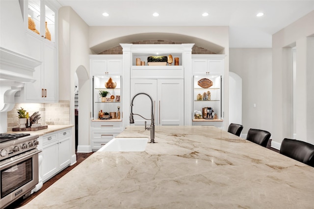 kitchen with sink, high end range, white cabinetry, a kitchen bar, and light stone countertops