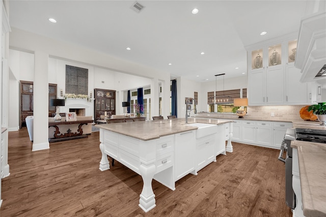 kitchen with light stone counters, pendant lighting, high end stainless steel range oven, a center island with sink, and sink