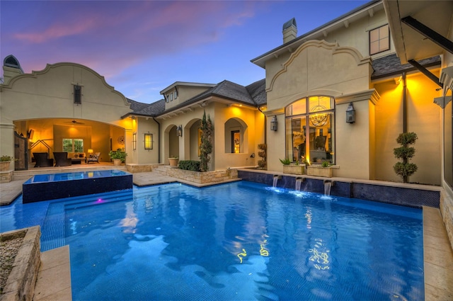 pool at dusk with pool water feature, a patio area, and ceiling fan