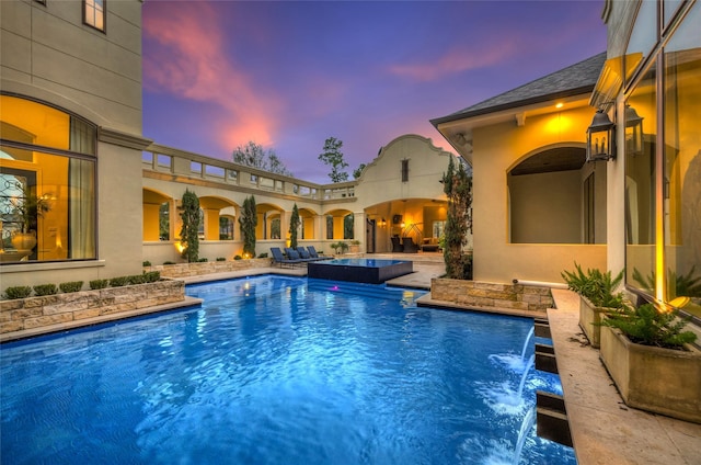 pool at dusk featuring an outdoor hangout area, a patio area, and pool water feature