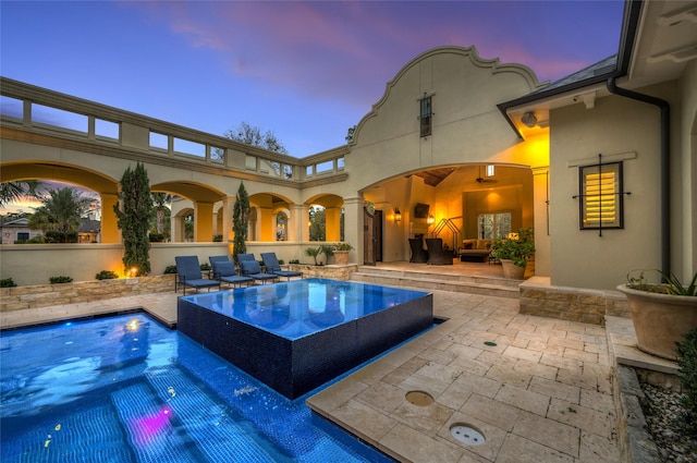 pool at dusk with an in ground hot tub and a patio area