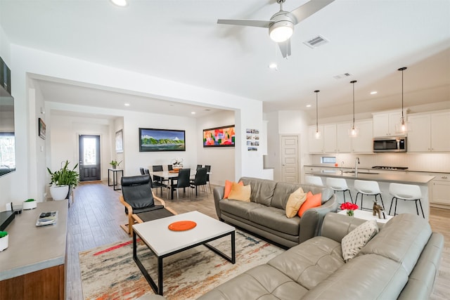 living room with ceiling fan, light hardwood / wood-style flooring, and sink