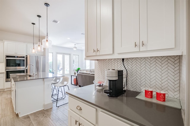 kitchen with pendant lighting, an island with sink, tasteful backsplash, white cabinetry, and stainless steel appliances