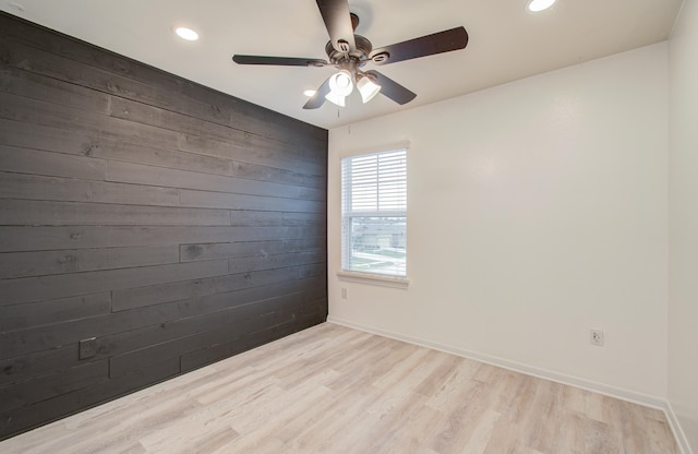 empty room with ceiling fan, wooden walls, and light hardwood / wood-style flooring