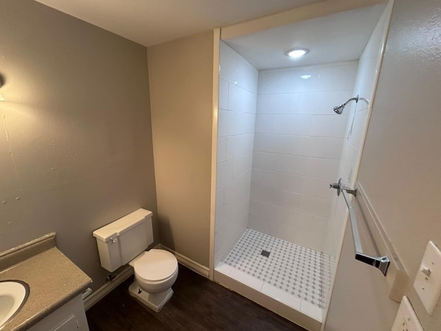 bathroom with a tile shower, vanity, wood-type flooring, and toilet