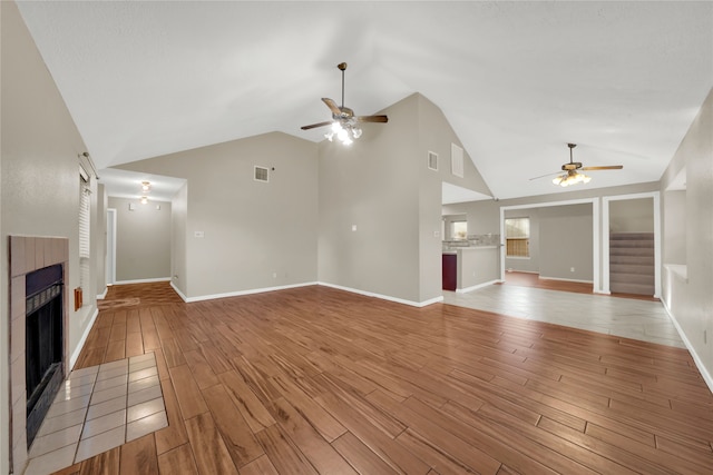 unfurnished living room with light wood-type flooring, vaulted ceiling, ceiling fan, and a tiled fireplace