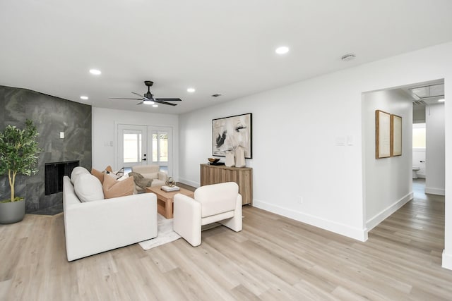 living room featuring light wood-type flooring, ceiling fan, and a premium fireplace