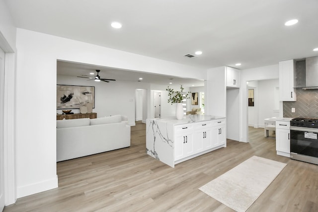 kitchen featuring white cabinetry, light stone countertops, wall chimney range hood, stainless steel range oven, and backsplash