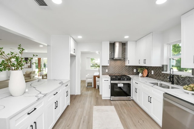 kitchen featuring light stone countertops, sink, stainless steel appliances, wall chimney range hood, and white cabinets