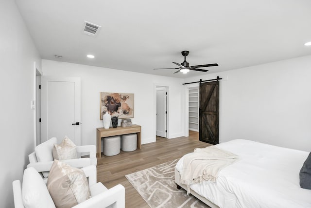 bedroom with a barn door, ceiling fan, and light hardwood / wood-style flooring