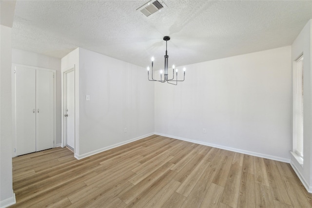 unfurnished dining area with a chandelier, a textured ceiling, and light hardwood / wood-style floors