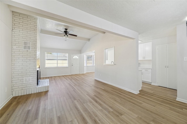 unfurnished living room featuring a brick fireplace, a textured ceiling, ceiling fan, light hardwood / wood-style flooring, and vaulted ceiling with beams