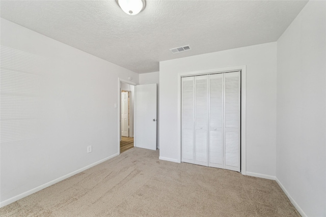 unfurnished bedroom featuring light carpet, a closet, and a textured ceiling