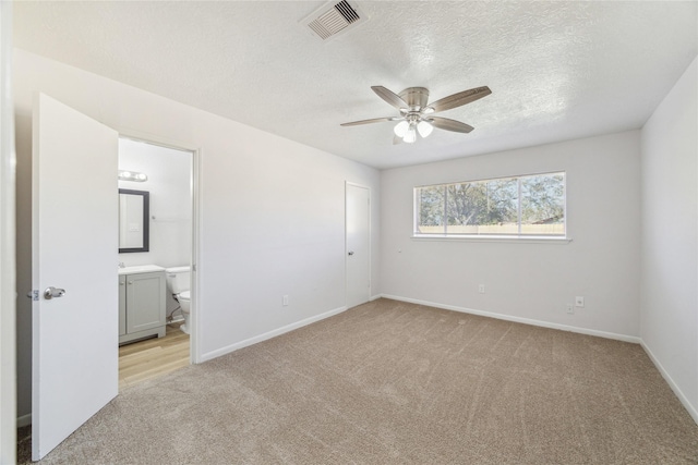 unfurnished bedroom with ceiling fan, light colored carpet, a textured ceiling, and connected bathroom