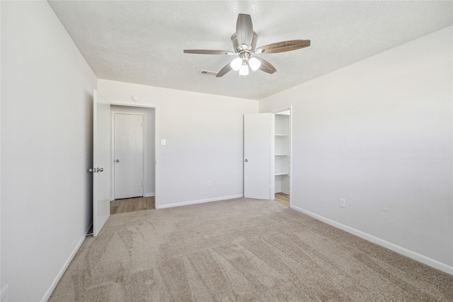 unfurnished bedroom with light carpet, a textured ceiling, ceiling fan, and a walk in closet