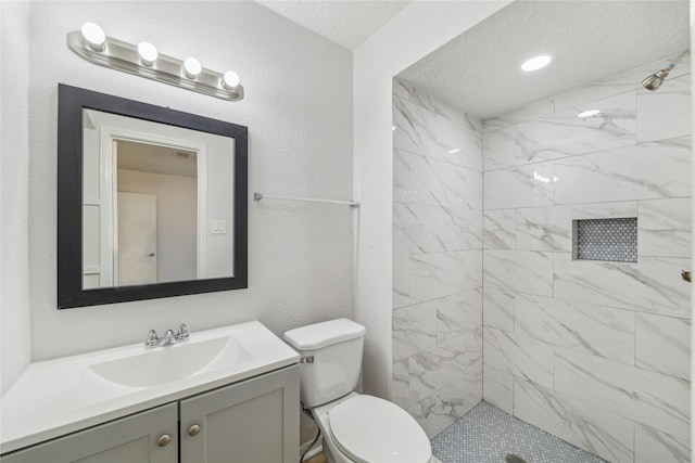 bathroom with vanity, a tile shower, a textured ceiling, and toilet