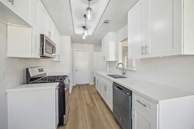 kitchen featuring sink, light hardwood / wood-style flooring, decorative light fixtures, white cabinetry, and stainless steel appliances