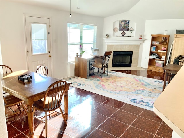 dining room featuring dark tile patterned flooring, lofted ceiling, and a tile fireplace