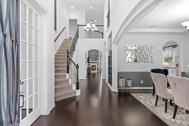 entrance foyer with arched walkways, a notable chandelier, ornamental molding, wood finished floors, and stairs