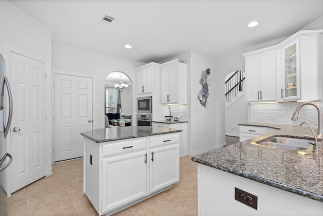 kitchen with visible vents, arched walkways, dark stone countertops, stainless steel appliances, and a sink