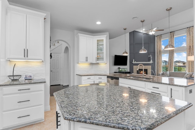 kitchen with arched walkways, a peninsula, a sink, a ceiling fan, and a center island