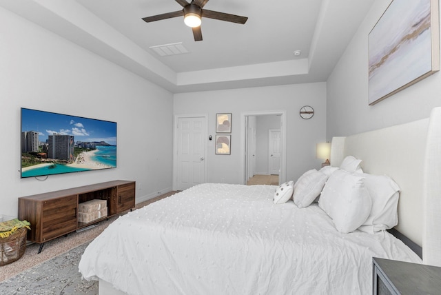 carpeted bedroom with a ceiling fan, a tray ceiling, visible vents, and baseboards