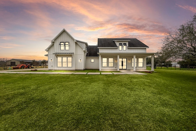 back house at dusk featuring a yard and covered porch