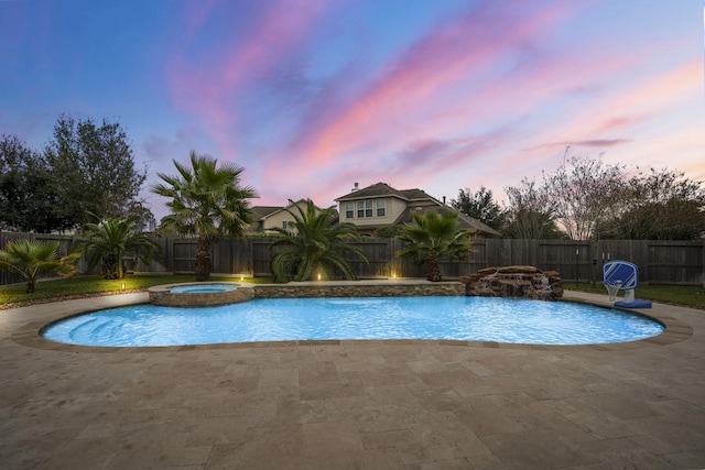 pool at dusk with pool water feature, an in ground hot tub, and a patio area