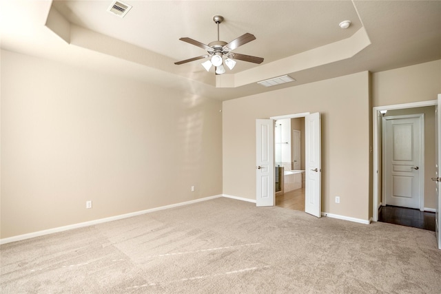 unfurnished bedroom featuring ceiling fan, light carpet, and a tray ceiling