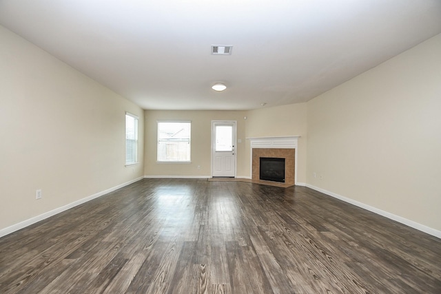 unfurnished living room featuring a tiled fireplace and dark hardwood / wood-style flooring