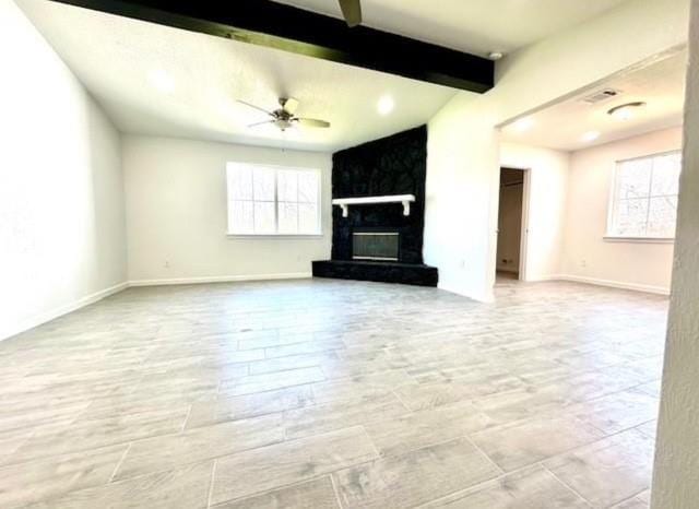 unfurnished living room with beam ceiling, a large fireplace, and ceiling fan