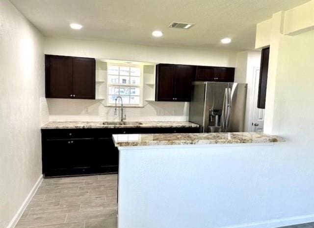 kitchen featuring stainless steel fridge, light stone counters, dark brown cabinetry, and sink