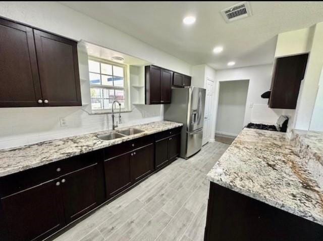 kitchen with light stone countertops, stainless steel refrigerator with ice dispenser, dark brown cabinetry, and sink