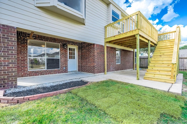 entrance to property featuring a lawn, a wooden deck, and a patio