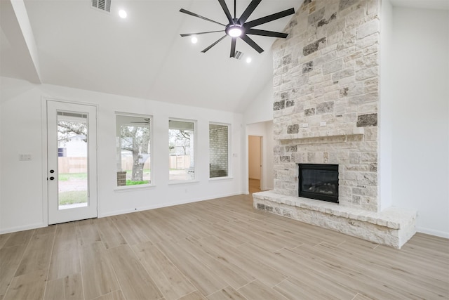 unfurnished living room featuring high vaulted ceiling, ceiling fan, a stone fireplace, and a wealth of natural light