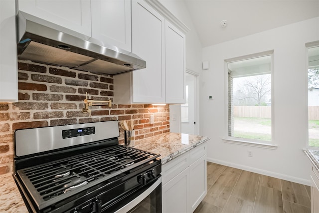 kitchen with exhaust hood, stainless steel gas range, light wood-type flooring, light stone countertops, and white cabinetry