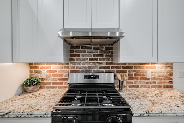 kitchen with white cabinets, wall chimney exhaust hood, light stone countertops, and gas range