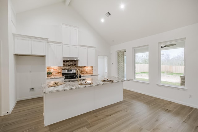 kitchen featuring light stone countertops, sink, beam ceiling, a center island with sink, and white cabinetry