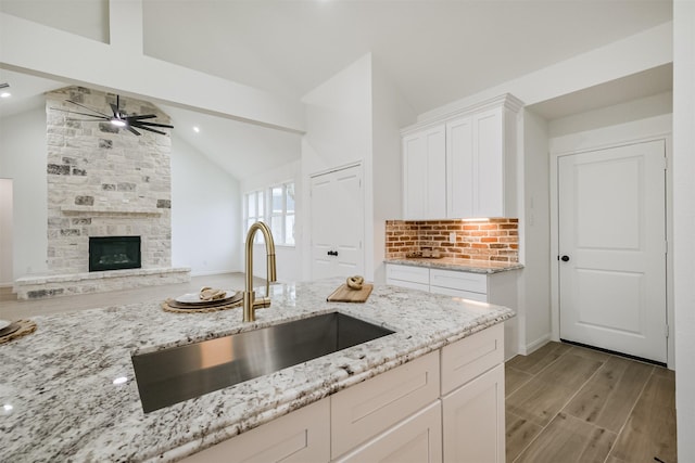 kitchen featuring lofted ceiling, white cabinets, sink, decorative backsplash, and light stone countertops